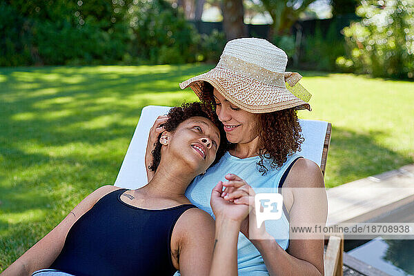 Happy affectionate lesbian couple cuddling on lounge chair in backyard