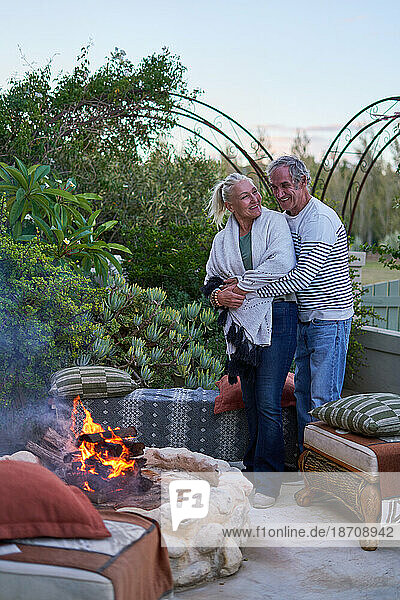 Happy senior couple hugging by fire pit on garden patio