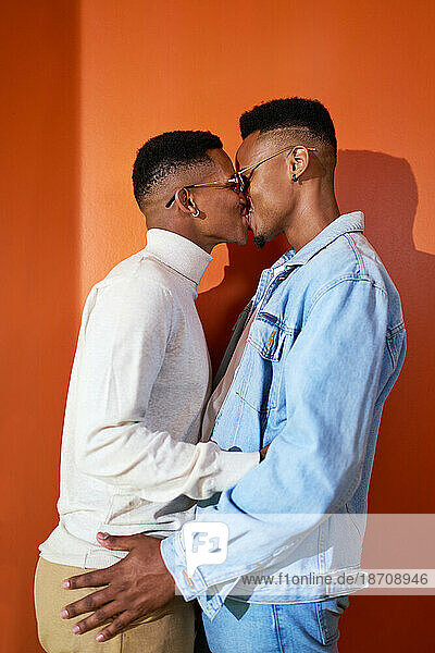 Portrait young gay male couple kissing on orange background