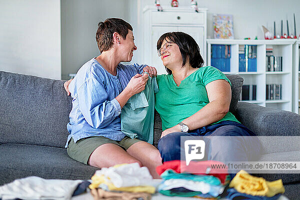 Happy lesbian couple talking and folding laundry on living room sofa