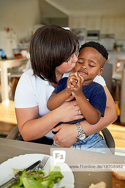 Mother kissing cute son eating at dinner table