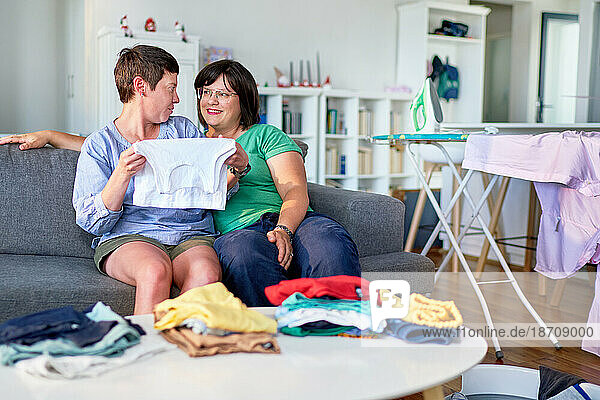 Happy lesbian couple folding laundry on living room sofa
