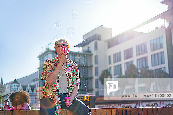 Young man blowing bubbles on sunny city urban balcony