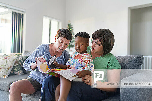 Lesbian couple and son reading book together on sofa at home