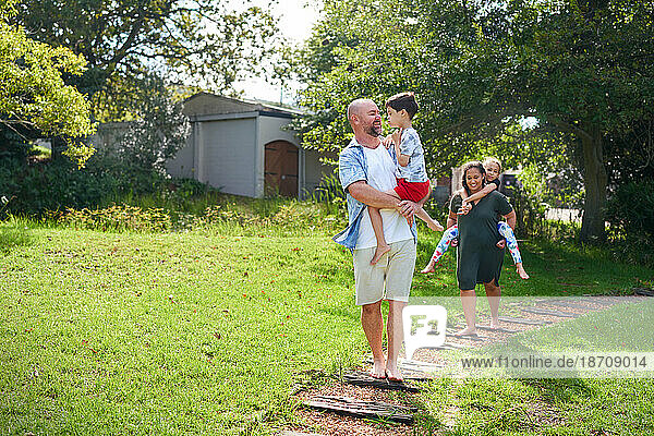 Happy parents carrying daughter and son on path in sunny backyard