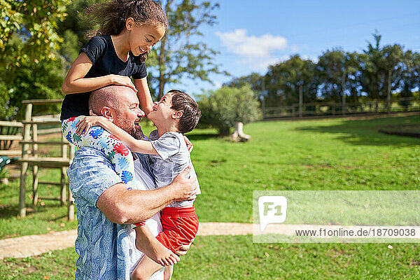 Father holding cute  playful kids in sunny summer park