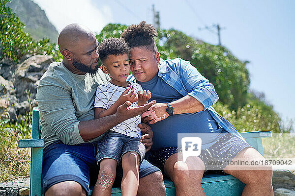 Gay male couple and son sitting on sunny beach bench