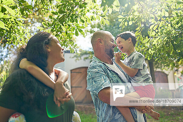 Happy parents and son with Down Syndrome below sunny tree