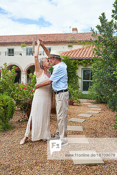 Happy senior couple dancing outside villa in summer garden