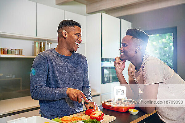 Happy young gay male couple cooking vegetables in kitchen at home
