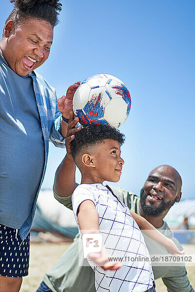 Happy gay male couple and son playing with soccer ball on sunny beach