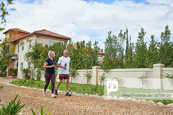 Active senior couple walking on footpath outside summer villa