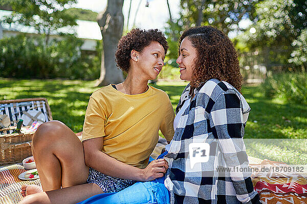 Happy lesbian couple talking on picnic blanket in summer park