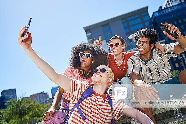Happy young friends taking selfie in sunny city park