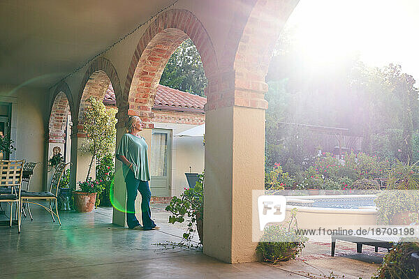 Serene  thoughtful senior woman standing on sunny villa patio