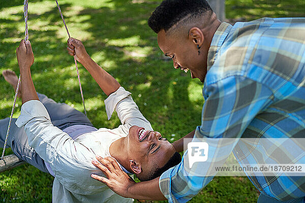 Happy young gay male couple on swing in summer park