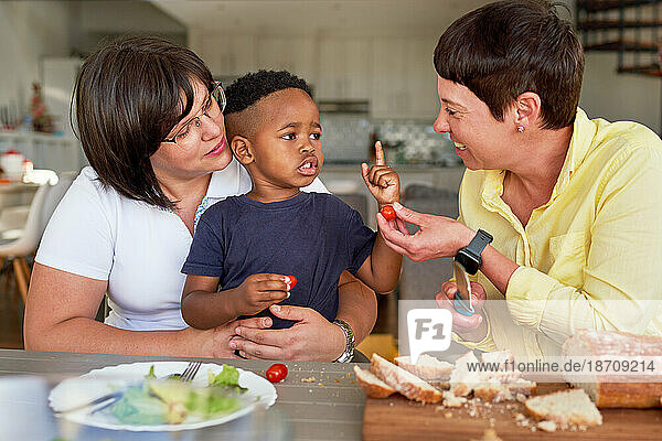 Lesbian couple and son talking  eating tomatoes at dinner table