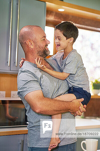 Father holding happy  cute son with Down Syndrome in kitchen