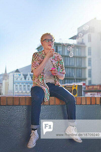 Young man blowing bubbles on sunny city balcony