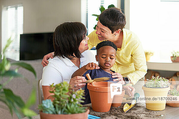 Happy lesbian couple and son planting plants in flowerpots at home