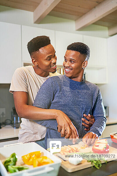 Happy  affectionate young gay male couple cooking and hugging at home
