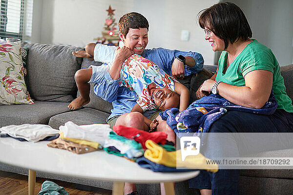 Happy lesbian couple folding laundry  tickling son on living room sofa