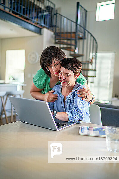 Happy lesbian couple using laptop together at dining table at home