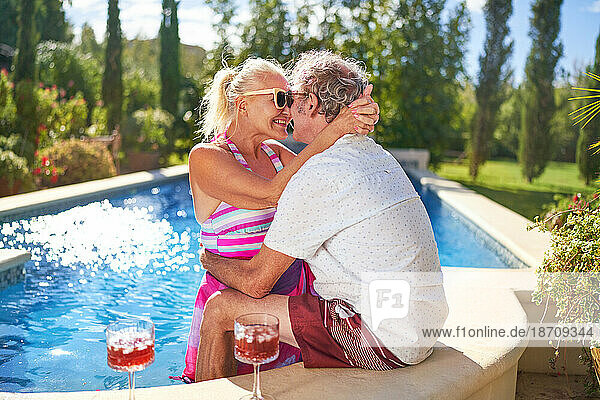 Happy senior couple hugging and kissing at sunny swimming pool