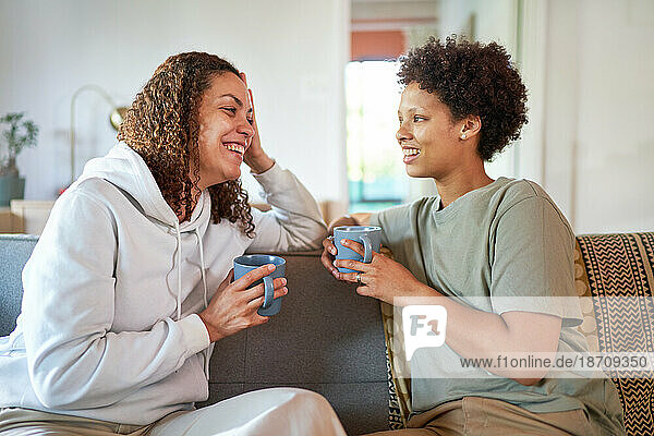Happy lesbian couple drinking coffee on living room sofa at home