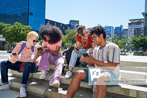 Young friends hanging out  using smart phones in sunny city park