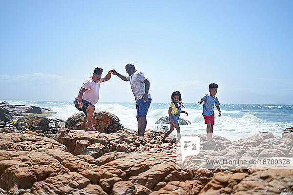 Gay male couple and kids walking on sunny ocean beach rocks