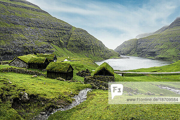 River flowing to the ocean crossing green meadows with grass-roof houses  Saksun  Streymoy Island  Faroe Islands  Denmark  Europe