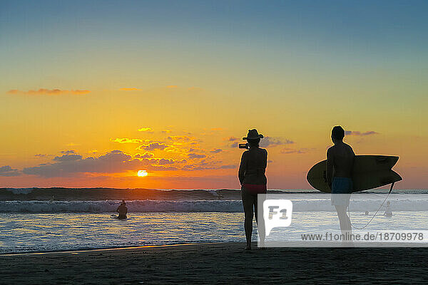 Surfer and woman photographing the sunset with smartphone on popular Guiones Beach  Playa Guiones  Nosara  Guanacaste  Costa Rica  Central America