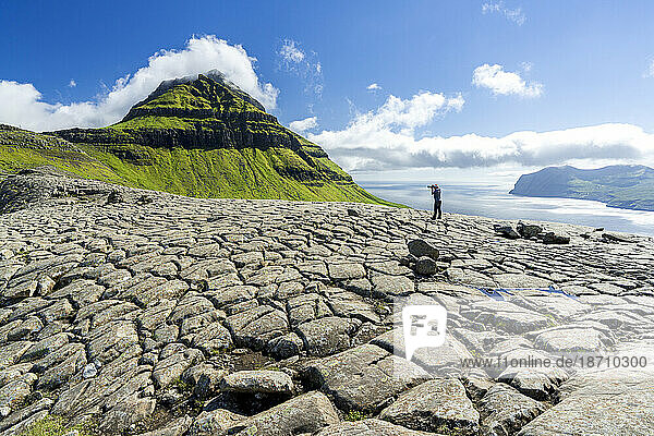 One tourist photographing Skaelingsfjall mountain standing on cracked soil in summer  Streymoy Island  Faroe Islands  Denmark  Europe
