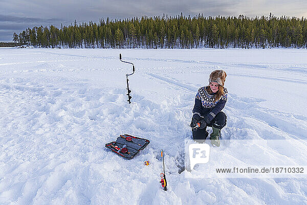 Woman in Scandinavian clothes ice fishing on a frozen lake  Lapland  Sweden  Scandinavia  Europe
