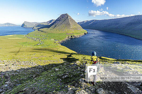 Hiker standing on top of hill with Vidareidi village and Malinsfjall mountain on background  Vidoy Island  Faroe Islands  Denmark  Europe