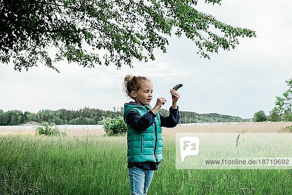 young girl stood in a field holding a feather looking happy