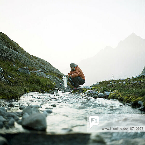 A man collects water during a hike in the mountains.