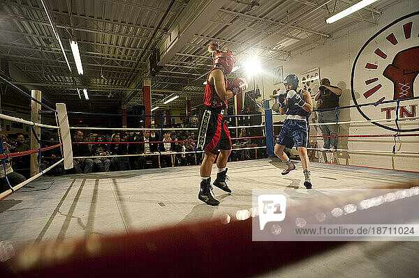 Two female boxers compete during a fight while judges and fans watch from edge of ring  Toronto  Ontario.