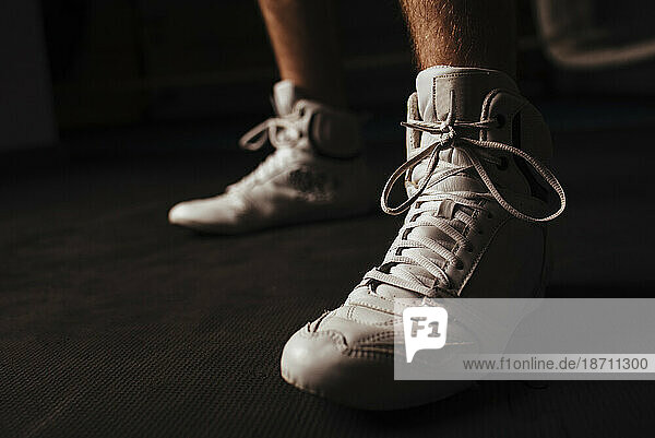 Closeup of white boxing shoes on dark background during workout.