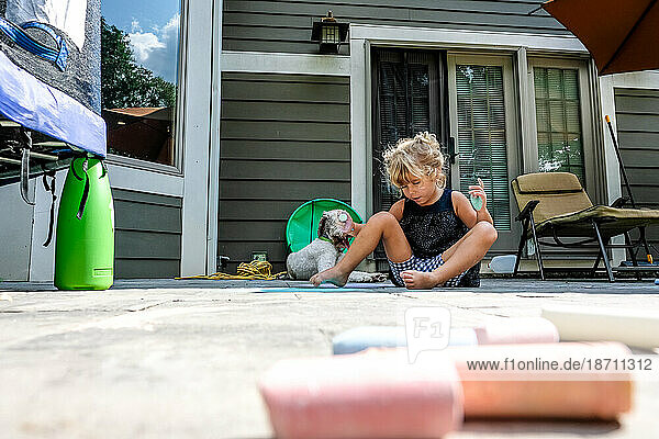 girl sitting on ground in backyard playing with chalk