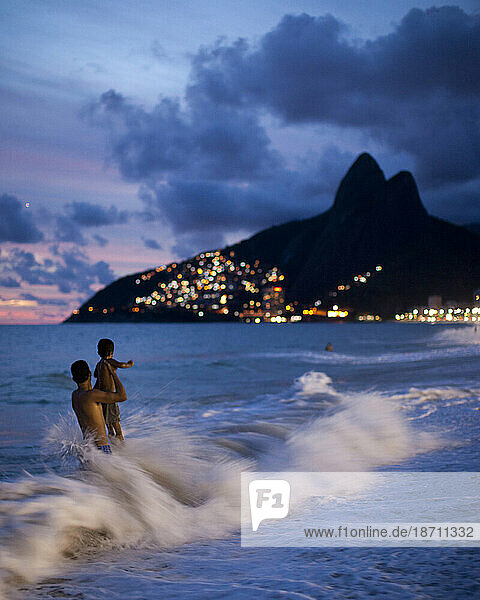 A man and child play in the waves on Ipanema Beach as the sun sets  Rio de Janeiro  Brazil.