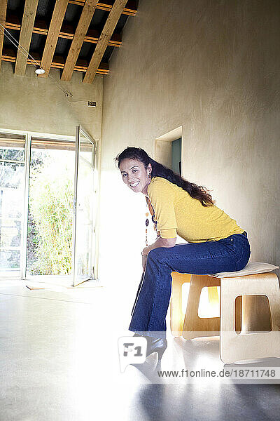 An Asian American woman sits on a bench inside a modern home in Del Mar  California.