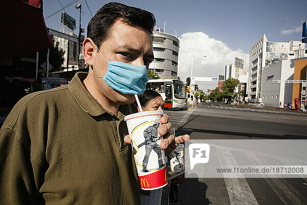 A man in the street drinks from a McDonald's cup through a blue mask during the swine flu epidemic in Mexico City.