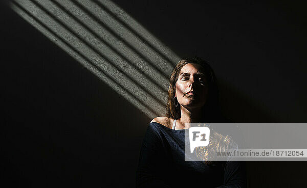 Portrait of a woman sitting in a patch of light with her eyes closed.