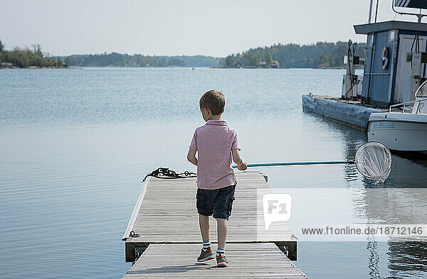 young boy standing on a jetty fishing with a net in the sea