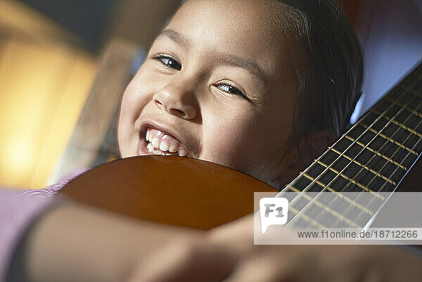 Little Asian girl holding her acoustic guitar and smiling into camera