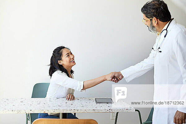 Mature male doctor doing handshake with female patient in clinic