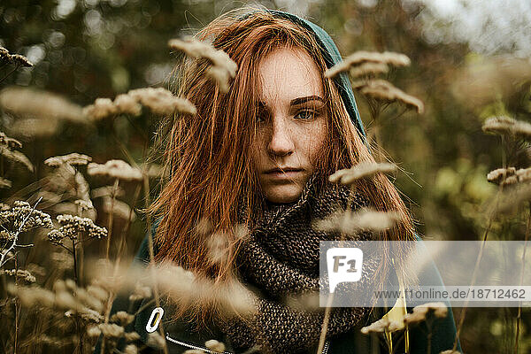 Thoughtful teenage girl with red head standing amidst plants