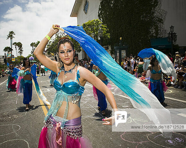 A harem dances up the street at a parade in Santa Barbara. The parade features extravagant floats and costumes.